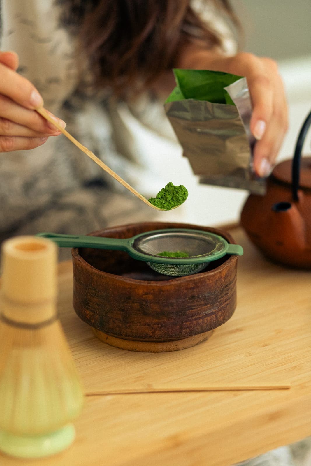 Matcha cernută într-un bol de ceramică, cu pămătuf și ceainic alături